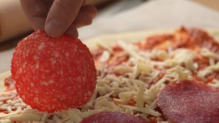 Placing Salami on Cheese Pizza. Close-up, shallow dof.