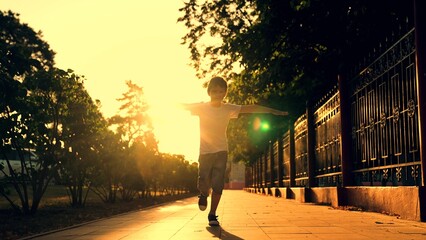 Joyful little boy runs at sunset in city park in spring. Child runs along sidewalk on street in sun. Children dream happiness concept. Happy child playing outdoors. Happy family. Child play, dreams