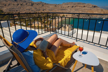 Woman reads a book on a balcony overlooking the sea.