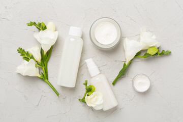 Facial cosmetic products with freesia flowers on concrete background, top view