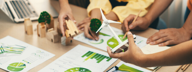 Windmill model represented using renewable energy placed during presenting green business on table with wooden block and environmental document scatter around. Closeup. Delineation. - obrazy, fototapety, plakaty