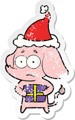 distressed sticker cartoon of a unsure elephant with christmas present wearing santa hat