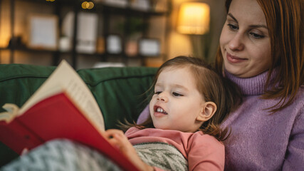 Mother and daughter toddler girl read book at home