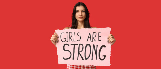 Young woman holding paper with slogan GIRLS ARE STRONG on red background. Feminism concept