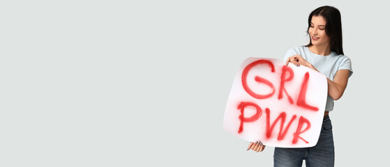 Young woman holding placard with slogan GRL PWR on light background with space for text. Feminism...