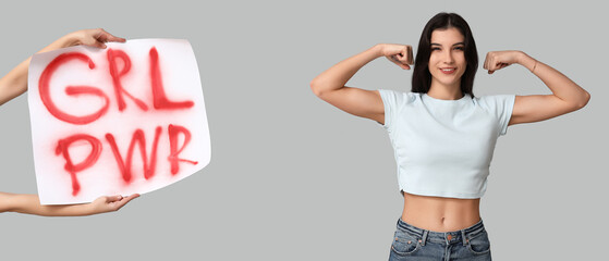 Young woman showing muscles and hands holding placard with slogan GRL PWR on grey background....