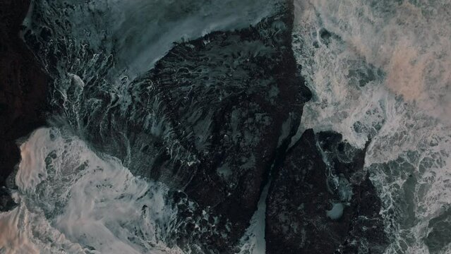 Aerial: Wild ocean crashing over rocks sunset during a storm. Piha, Auckland, New Zealand