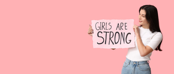 Young woman holding paper with slogan GIRLS ARE STRONG on pink background with space for text....