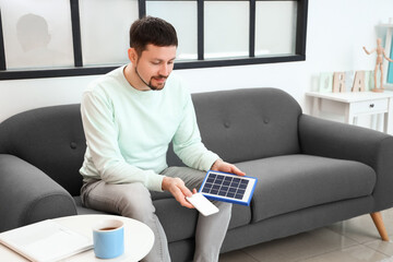 Handsome man with portable solar panel and mobile phone at home