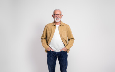 Fototapeta premium Portrait of smiling confident senior businessman with hands in pockets posing on white background