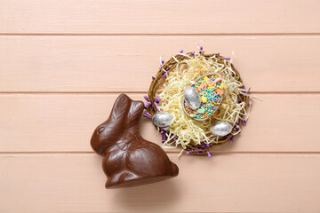 Easter bunny with wreath and chocolate egg full of sprinkles on pink wooden background