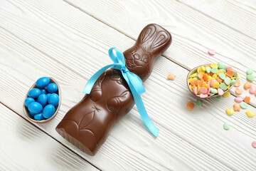 Chocolate Easter eggs with sprinkles, candies and bunny on white wooden background