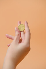 Fototapeta na wymiar A women's hand holding a 50 euro cent coin, on an orange background, close-up