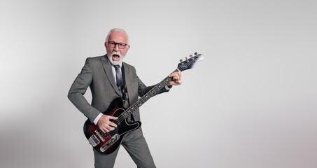 Fototapeta premium Excited senior rock musician in suit singing with mouth open and playing guitar on white background