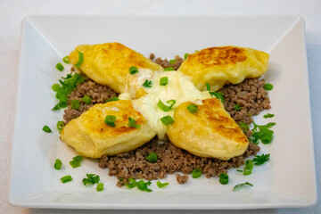 Traditional Ukrainian pierogi grilled in butter and served with minced meat and cream, decorated with fresh fine herbs