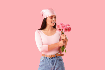 Beautiful young Asian woman with bouquet of dahlias on pink background