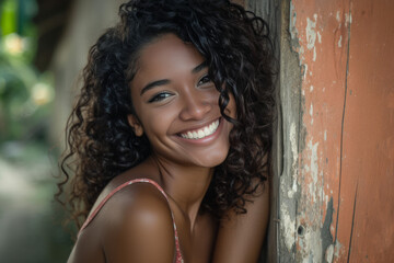 A woman with curly hair leans against a wall and smiles