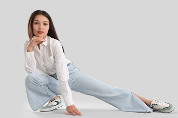 Young Asian woman in trendy jeans on light background