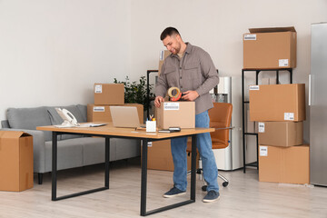 Male seller packing parcel box with tape in warehouse store