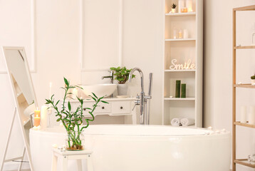 Interior of light bathroom with burning candles, bathtub and mirror