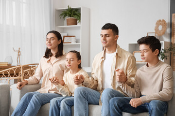 Family praying on sofa at home