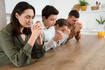 Family praying together at table in kitchen
