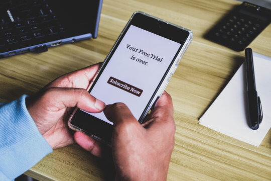 Person using mobile phone displaying your free trial is over subscribe now message. Selective focus.