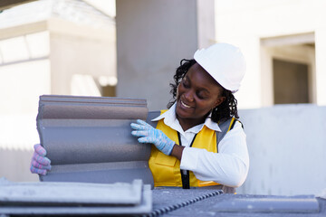An African American female contractor is examining rooftop tiles at the construction site. 