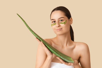 Beautiful young happy woman with aloe vera on beige background
