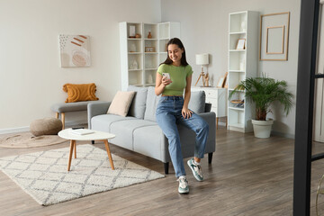 Young woman using mobile phone on grey sofa in living room