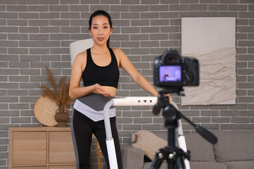 Female Asian sports blogger on treadmill recording training video at home