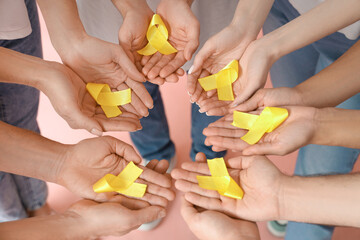 People with yellow awareness ribbons on pink background, closeup. World Cancer Day