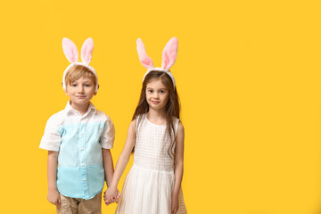 Cute little children in bunny ears holding hands on yellow background