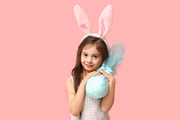 Cute little girl in bunny ears with Easter gift egg on pink background