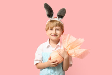Cute little boy in bunny ears with Easter gift egg on pink background
