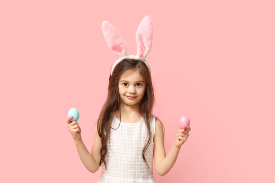 Cute little girl in bunny ears with Easter eggs on pink background