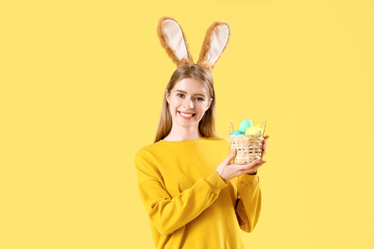 Young woman in bunny ears with Easter eggs on yellow background