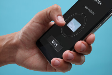 Got new message. Man using smartphone on light blue background, closeup