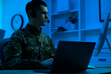 Military service. Soldier in headphones working at table in office at night - obrazy, fototapety, plakaty
