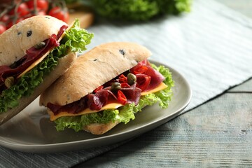 Delicious sandwiches with bresaola, cheese and lettuce on light blue wooden table, closeup. Space for text