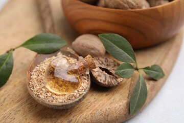 Nutmeg essential oil, whole and ground nuts on wooden board, closeup