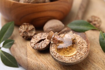 Nutmeg essential oil, whole and ground nuts on wooden board, closeup