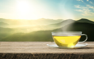 Aromatic green tea in glass cup on wooden table in mountains, space for text