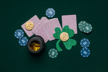 Poker chips, cards, clover and pot with coins on dark green background. St. Patrick's Day...