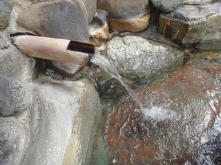 Traditional japanese onsen outdoor stone bath tub, water flowing from hot spring wooden fountain