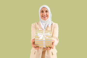 Mature Muslim woman with gift box on green background. Ramadan celebration