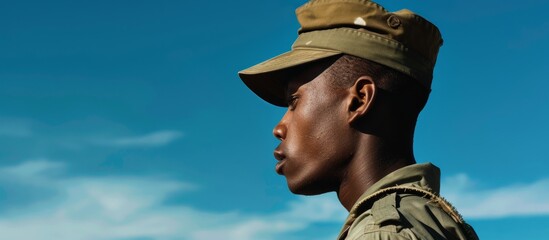 African American soldier in cap seen from the side with a blue sky in the background. - obrazy, fototapety, plakaty