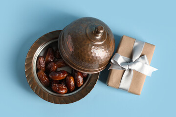 Gift box and bowl with dried dates for Ramadan on blue background