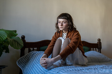 Unemotional introverted teenager with empty glance sitting on bed alone at home. Unhappy sed girl...