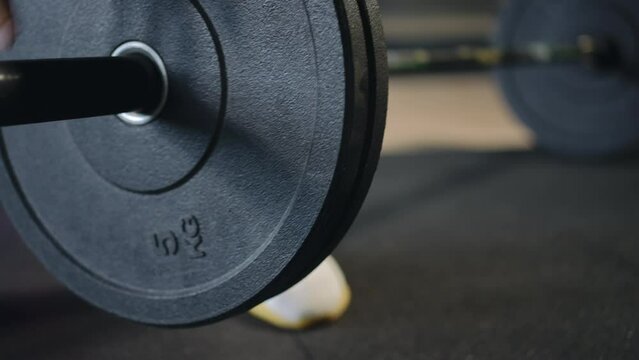 Close-up of a barbell on which an unrecognizable man puts an additional barbell plate on and then lifts it